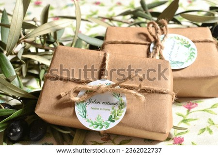 Small gifts packaging natural organic olive oil soaps wrapped in brown craft paper rustic style jute ribbon on olive leaves background, wedding decoration, labels translation handmade natural soap