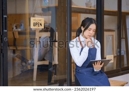 Unhappy and upset female entrepreneur sitting at her shop with an open signboard on the glass door.