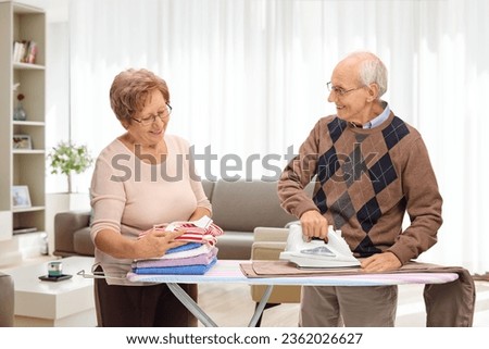 Senior couple ironing together at home in a living room