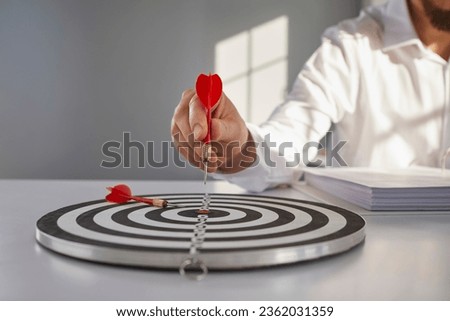 Confident businessman or financial entrepreneur points red arrow right in bulls eye of shooting archery circle target on grey office desk. Hand holding arrow in close up. Setting business goal concept Royalty-Free Stock Photo #2362031359