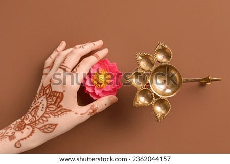 Female hand with diya lamp and lotus flower for celebration of Divaly on brown background