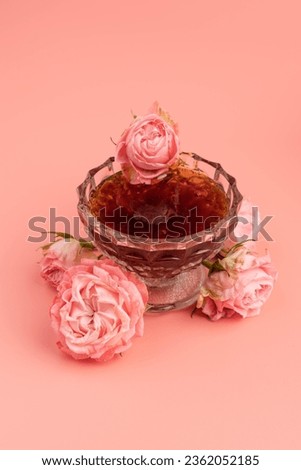 Glass little bowl with tea rose petal jam on pink background. Copy space for text.