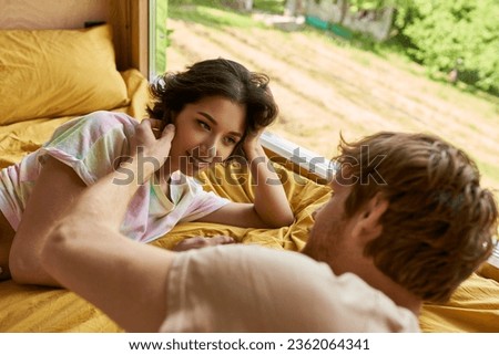 tender gesture, redhead man touching cheek of asian woman and lying on bed together in morning Royalty-Free Stock Photo #2362064341