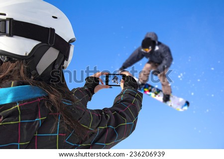 A young girl by mobile phone photographed of snowboarder jump