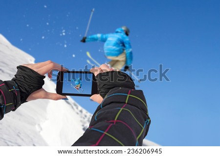 A young girl by mobile phone photographed of skiers jump