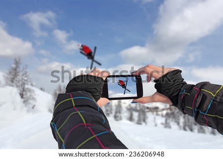 A young girl by mobile phone photographed of skiers jump