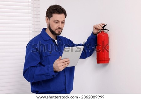 Man with tablet checking fire extinguisher indoors Royalty-Free Stock Photo #2362089999