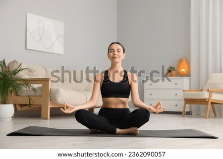 Beautiful young woman practicing Padmasana on yoga mat at home. Lotus pose