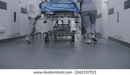 Doctors and nurses run and push stretcher with seriously injured patient to operating room. Medics save human life. Close up of medical personnel legs. Bright medical facility corridor. Slow motion. Royalty-Free Stock Photo #2362107921