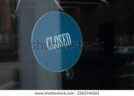 Text Closed is covered on round blue sign behind glass door of store. Signal board. Reflection. Concept, lateness, closure, border, end of process, labor mode. Error 404. No light. Window of city cafe