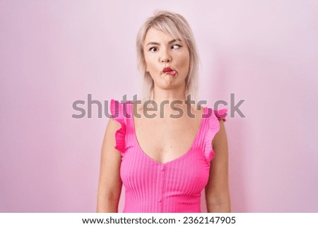 Young caucasian woman standing over pink background making fish face with lips, crazy and comical gesture. funny expression. 