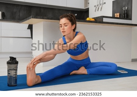 Fitness and workout concept. Young woman stretching her legs, doing exercises at home on yoga mat, doing splits on floor in living room.