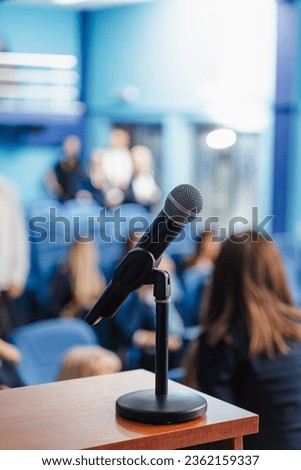 Blurred background of students, professors or business people waiting for speech at conference hall. Focus on microphone.