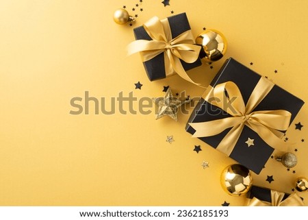 Luxurious New Year's presents: Overhead image of exquisite black gift boxes with gold bows, paired with baubles, star decorations, confetti against yellow surface, space for greeting or advertising