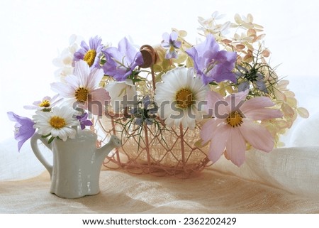 Bouquet of cosmos flowers, hydrangea, bells, pansies, nigella in a basket and watering can on a table, a beautiful summer and autumn still life, postcard.