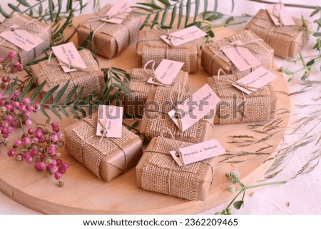 Autumn fall wedding decoration guest gifts rustic style soaps wrapped in brown craft paper jute fabric ribbon and custom labels with names, wodden table background with red berries and green leaves