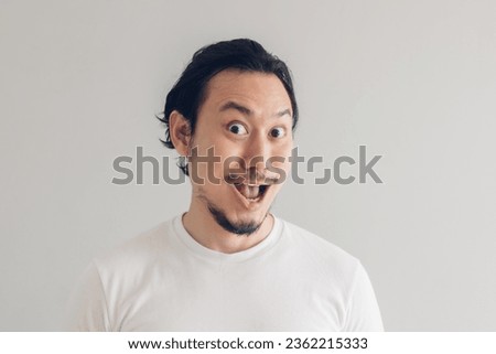 Funny grinning smile face of Asian man in white t-shirt and grey background. Royalty-Free Stock Photo #2362215333