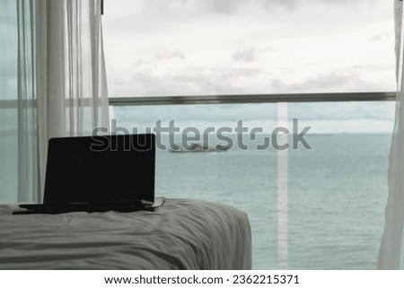 Workation concept. Empty screen laptop on bed with ocean view balcony.