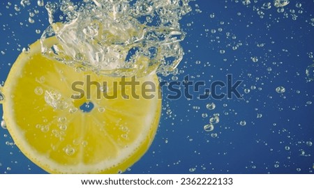 Underwater lemon slice in soda water or lemonade with bubbles. Refreshing soda tonic fizzy cocktail. Close up of lemons and ice cubes in glass. Lime in splashing sparkling water cold drink beverage.