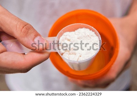 A close-up of a measuring cup of protein powder next to a shaker. Protein supplementation, healthy lifestyle