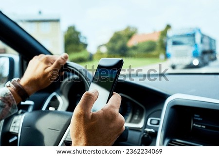 Young man using his smartphone while driving his car in the city