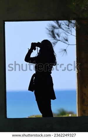 Silhouette of a woman bird watching on the beach with binoculars. silhouette of a woman observing a bird.