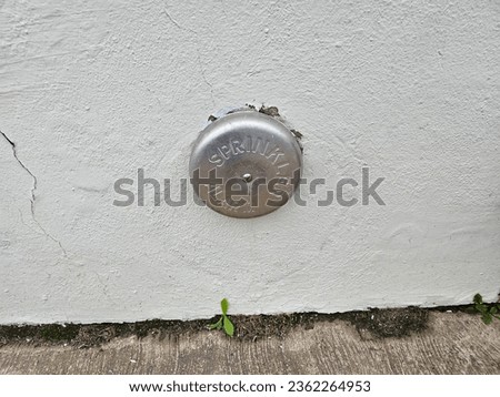 A metal sprinkler alarm in the side of a wall.