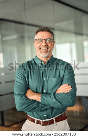 Happy older business man executive standing in office arms crossed, vertical portrait. Smiling mature banker, confident middle aged professional businessman manager entrepreneur looking at camera.