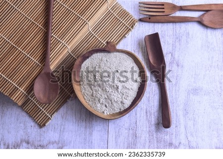 Chicken stock powder inside wooden bowl on the side of sushi roller with wooden spoons and fork on top of table
