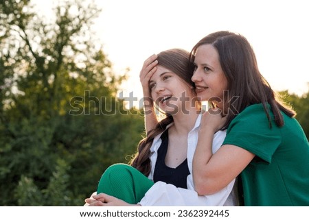 Mom and teenage daughter are hugging on a walk in the park. Good parent-teen relationship