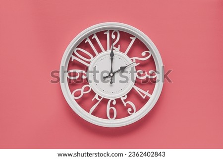 Modern white clock with a circle on a pink wall background, two o'clock on the clock. Elegant clock in the modern style, combination of white and pink colors