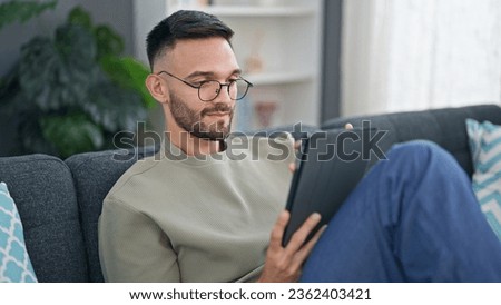 Young hispanic man using touchpad sitting on sofa at home