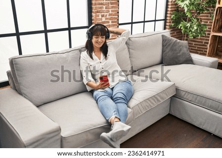 Young beautiful hispanic woman listening to music sitting on sofa at home