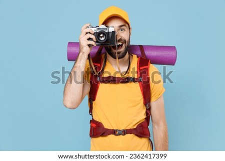 Excited young traveler man in t-shirt cap backpack isolated on blue background. Tourist traveling on weekend getaway. Tourism discovering hiking concept. Taking pictures on retro vintage photo camera