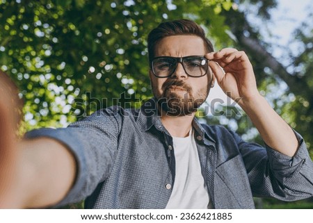 Close up young cool stylish man 20s in blue shirt touching glasses do selfie shot on mobile cell phone relax in spring forest garden green city park outdoors on nature Urban lifestyle leisure concept