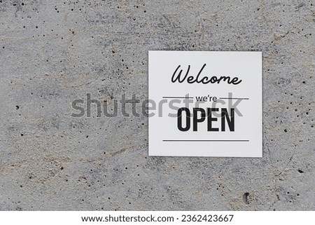 Text on vintage white sign " welcome we' are Open" in cafe. on cement wall background.	
