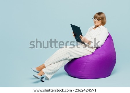 Full body employee business woman 50s wearing white classic suit glasses formal clothes hold clipboard with paper account documents isolated on plain pastel blue background. Achievement career concept