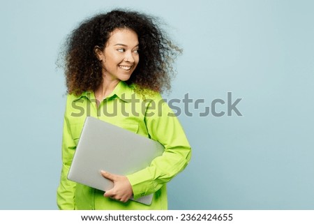 Side view smiling young IT latin woman she wear green shirt casual clothes hold use work on laptop pc computer look aside isolated on plain pastel light blue cyan background studio. Lifestyle concept
