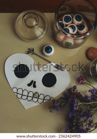 halloween still life with a jar of eyeballs, candles, insect and a heart shaped skull card