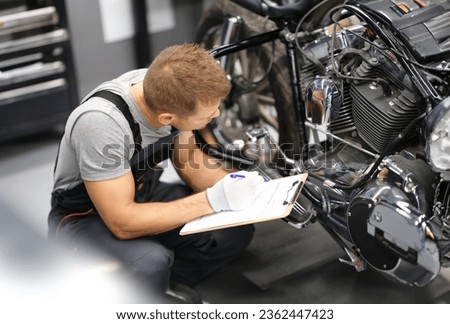 Foreman in service repair center diagnoses parts on motorcycle. Service and warranty service of concept motorcycles Royalty-Free Stock Photo #2362447423
