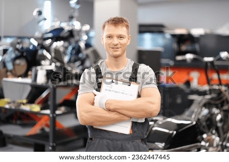 Handsome auto mechanic posing in car service and holding documents in hands. High-quality service of auto technics concept Royalty-Free Stock Photo #2362447445