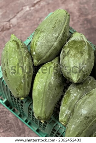 a photography of a crate of cucumbers on a table, acorn squash in a green crate on a table.