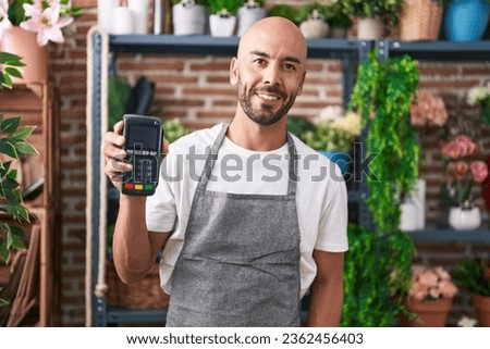 Middle age bald man working at florist shop holding dataphone looking positive and happy standing and smiling with a confident smile showing teeth 