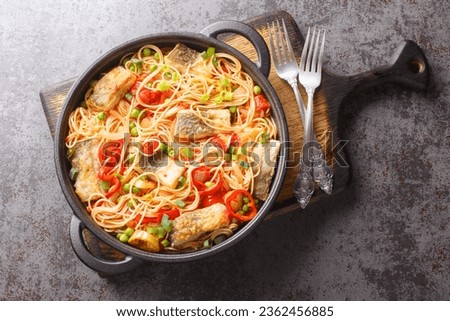 Main course spaghetti with white fish fillet, peppers, onions, green peas and tomato sauce close-up in a frying pan on the table. Horizontal top view from above
