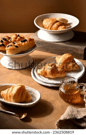 Cafe menu, breakfast. Fresh pastries: croissants, rolls, puffs and raisin bun with sour cream in plate adn bowl. Bird of view, with napkin and wooden background Royalty-Free Stock Photo #2362508819