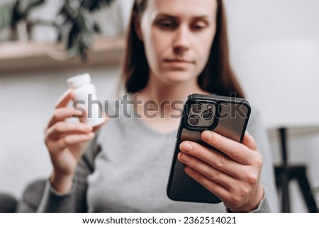 Selective focus of young lady using smartphone for reading, searching prescription on bottle medicine, pill label text about information online, instructions side effects, pharmacy medicament concept Royalty-Free Stock Photo #2362514021