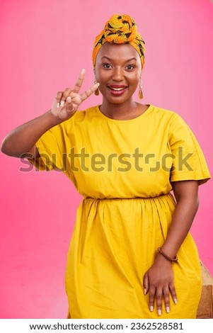 Black woman, peace sign and smile in studio portrait with fashion, emoji or hand icon by pink background. African girl, yellow dress and happy with v, vote and opinion for success with trendy style Royalty-Free Stock Photo #2362528581
