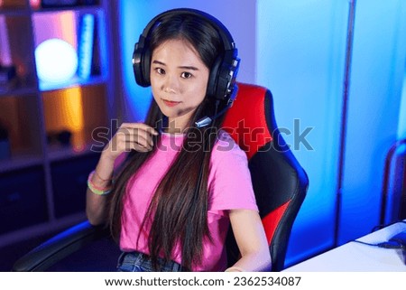 Young chinese woman streamer smiling confident sitting on bed at gaming room