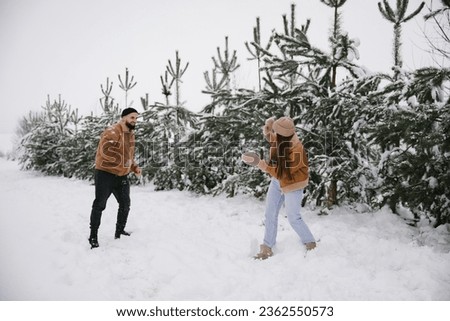 A couple in love plays snowballs in the winter in the forest for a walk. Happy couple have fun in winter near snow-covered pines.