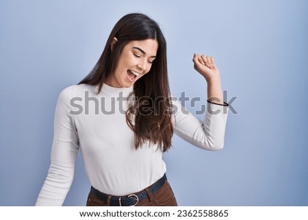 Young brunette woman standing over blue background dancing happy and cheerful, smiling moving casual and confident listening to music 